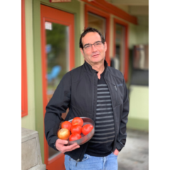 man in black jacket holding a bowl of tomatoes